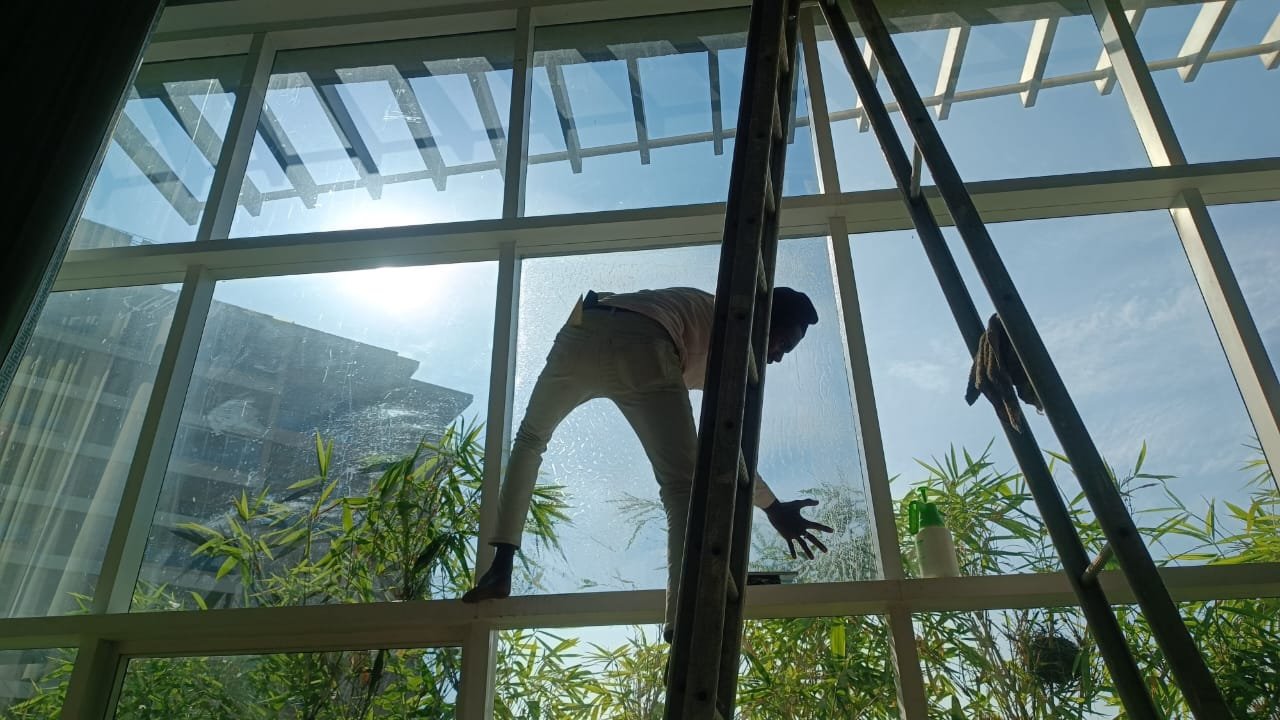 Installer applying film on tall glass window using ladder